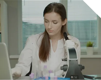 Female medical staff in a lab coat looking trough a microscope and writing down something